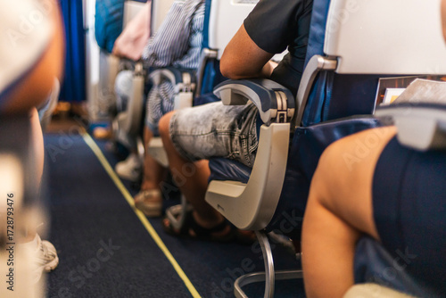 Travelers are sitting in an airplane cabin, focused on their surroundings. The image captures diverse clothing styles and relaxed body language as the flight progresses