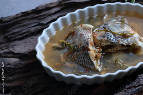 Tilapia Fish Tom Yum, Tom Yum Tilapia Fish Creamy river prawn spicy soup Recipe in a white plate on a wooden background