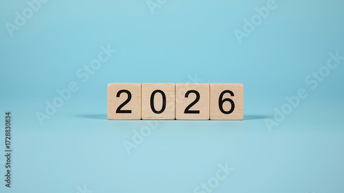 2026 Happy New Year concept with wooden cube blocks changing from 2025 to 2026 on blue background, minimal design symbolizing time change and new beginnings.
