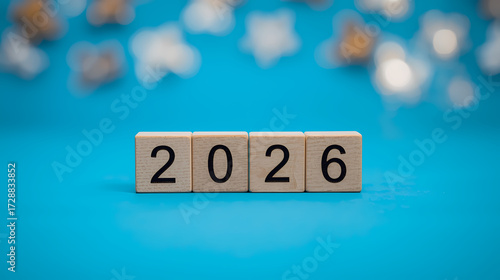 Professional photo of 2026 Happy New Year wooden cube blocks transitioning from 2025, on vibrant blue background with minimal modern holiday celebration design.