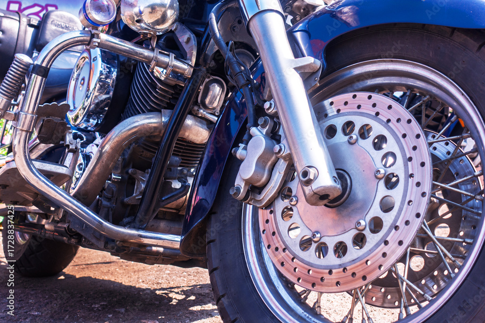 Obraz premium Close-up of a classic cruiser motorcycle's front wheel, showcasing the shiny chrome engine, disc brake, and detailed mechanical components. Evokes freedom, power, and the open road.