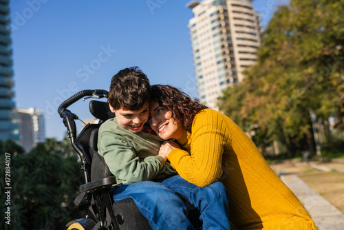 Mother hugging son in wheelchair at park