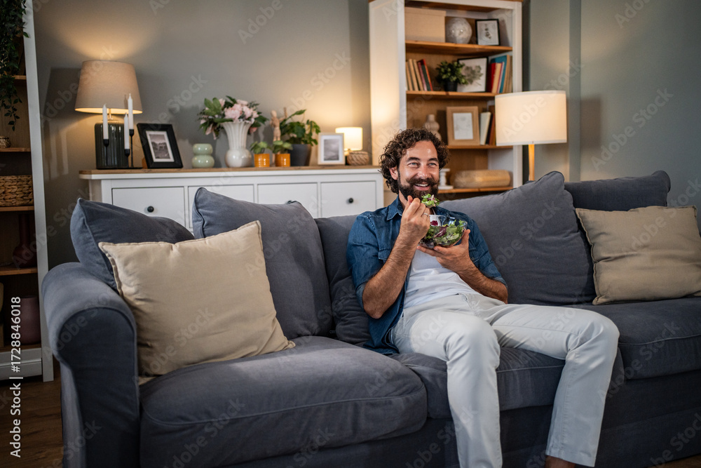 Obraz premium Man relaxing on couch eating healthy salad