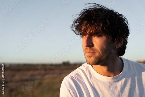 Fotografie Man with curly hair contemplating outdoors during sunset, feeling peaceful and e