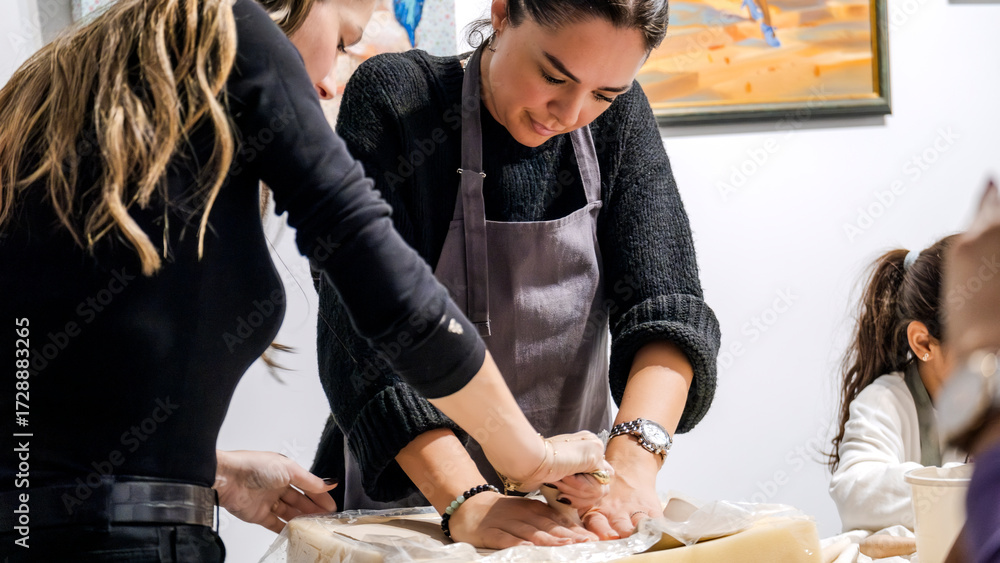 Fototapeta premium In an art studio two beautiful middle-aged artist friends are working on clay shaping at a table