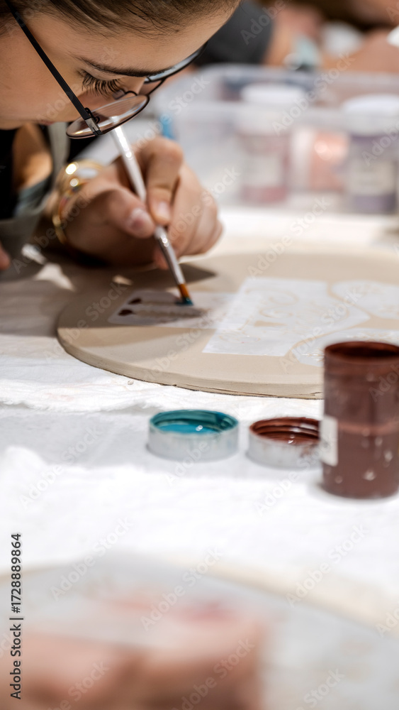 Fototapeta premium In an art studio during an art event, a young girl child is painting a shape she made from clay