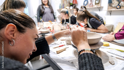 In an art studio with an environment adorned with artistic paintings in the background, two beautiful middle-aged artist friends are working on clay shaping at a table
