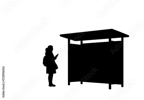 Silhouette of a person at a bus stop using a mobile phone.
