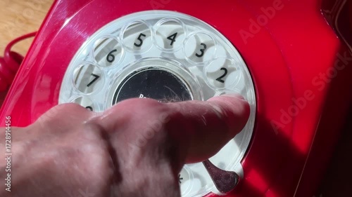 close up of a hand dialing 911 on a bright red rotary dial telephone