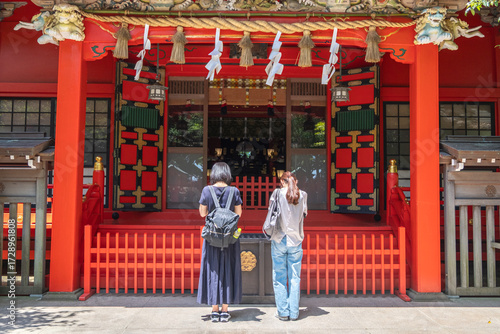 Two women praying at traditional Japanese shrine entrance outdoors at Enoshima, Kamakura, Kanagawa, Japan