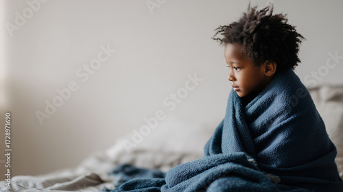 Sad black american child 6 years old wrapped in blanket sitting on bed