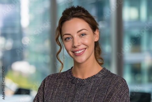 Portrait of a smiling woman with curly brown hair in front of a blurred office building window