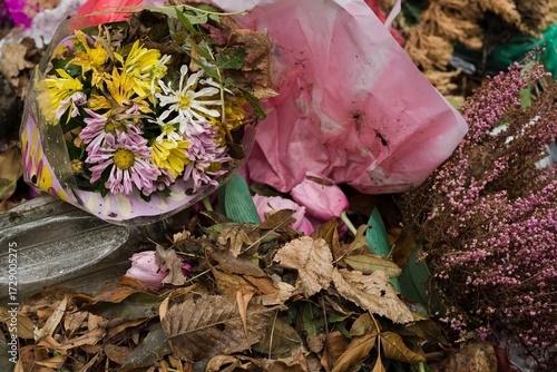 Discarded flowers with dry leaves and plastic waste in cemetery container