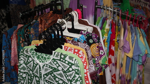 Colorful batik shirts hang on a rack in a local market, showcasing traditional patterns and vibrant colors, creating a lively and cultural atmosphere.