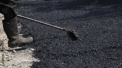 Worker spreading fresh asphalt on a road construction site, creating a smooth surface for new pavement and infrastructure development.