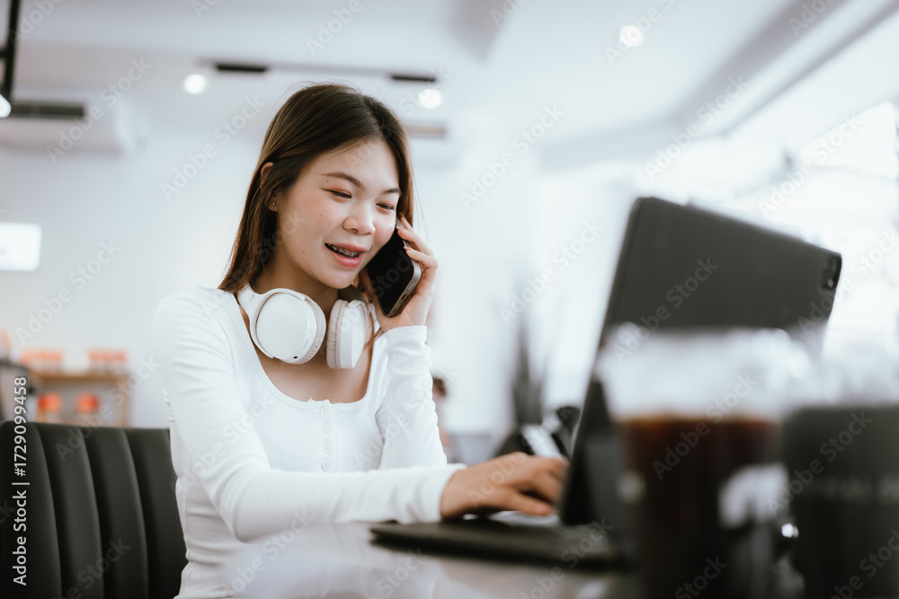 Obraz premium Smiling young woman with braces wearing headphones, working on laptop at cafe, enjoying online learning or remote work.