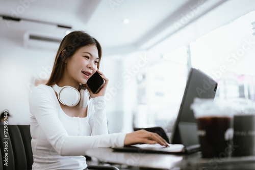 Smiling young woman with braces wearing headphones, working on laptop at cafe, enjoying online learning or remote work.
