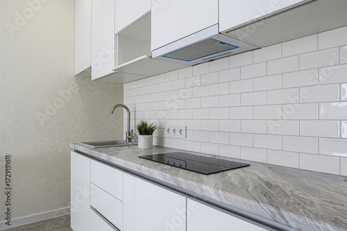 A modern kitchen features white cabinets, a gray marbled countertop, white subway tile backsplash, and stainless steel fixtures. Clean and stylish