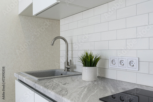 Modern kitchen detail: grey sink, marble countertop, white subway tiles, green plant, and a triple outlet. Clean and minimalist design