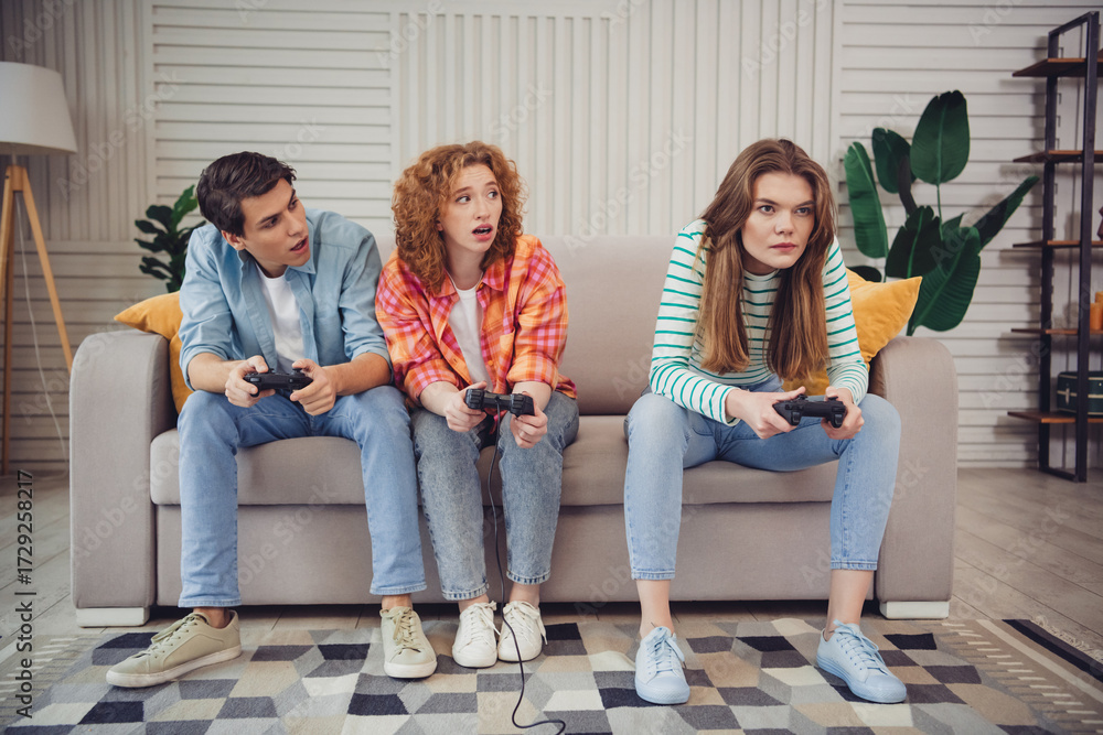 Obraz premium Funny young people engaged in a video game competition, sitting on a cozy couch in a modern living room.