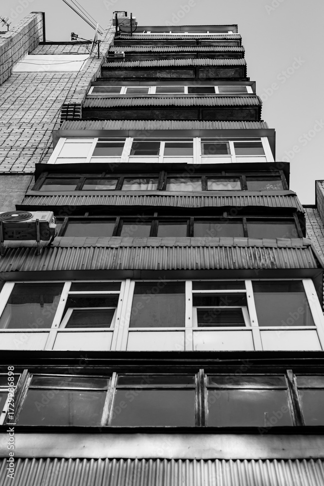 Obraz premium Stark, worm's-eye view of old residential balconies stacked high on an apartment building. Gritty, urban geometry in black and white.