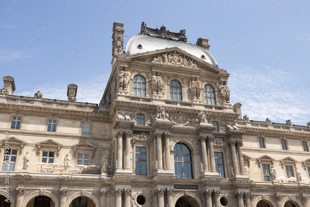 Fototapeta premium Architectural masterpiece showcasing intricate details of a historic building with ornate sculptures, large windows, and a majestic roof under a clear blue sky, symbolizing cultural heritage