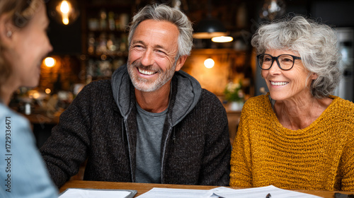 Happy senior couple smiling while talking with advisor at table, symbolizing retirement planning, financial advice, trust, communication, and positive lifestyle. 
