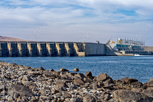 The rocky shoreline of the Columbia River faces the Wanapum dam spillway and powerhouse in Washington, USA