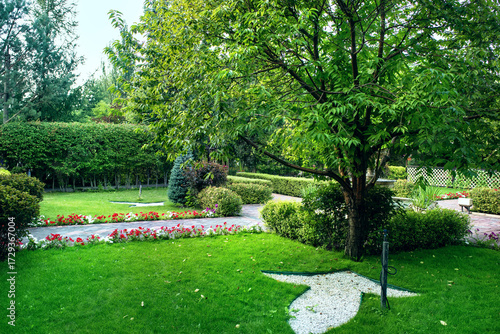 A beautiful garden landscape with a green lawn, hedge, bushes and trees.