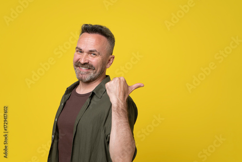 Handsome middle age hoary senior man isolated over yellow background Pointing to the back behind with hand and thumbs up, smiling confident.