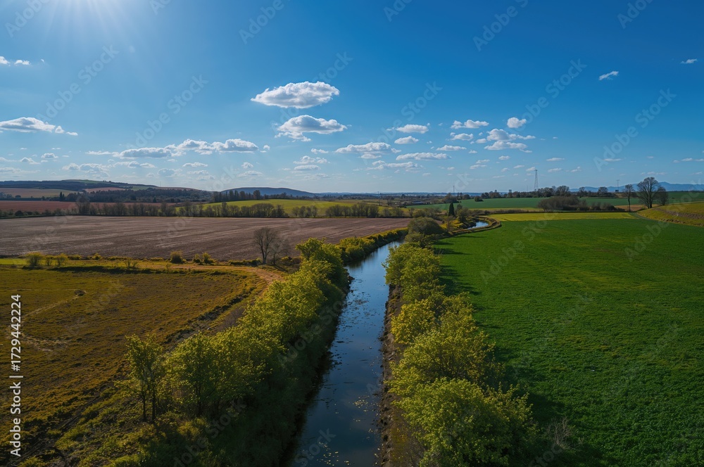 Obraz premium Aerial perspective of an empty irrigation channel in farmland. Rural scenery with clear skies and lush greenery.