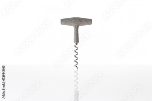 A metallic corkscrew with a textured handle is positioned vertically in the middle of the frame, resting on a smooth, reflective surface with a bright, plain backdrop.