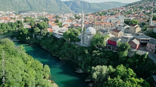 Mostar, Bosnia and Herzegovina  Aerial drone video moving along the Neretva River, bypassing Koski Mehmed Pasha Mosque, and centering on Sinan Pasha Mosque with hills and Mostar city in the background