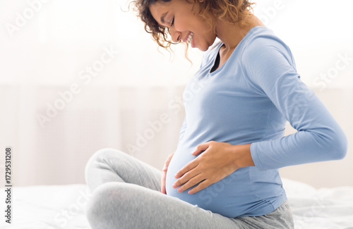 Happy expectant woman touching belly, enjoying unborn baby pushings in bed, side view