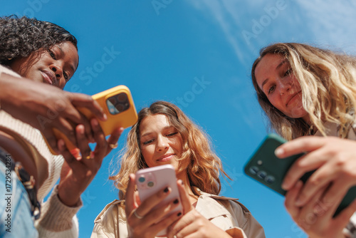 Group of young women holding smartphones, looking down at screens from a low angle