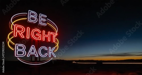 Glowing red and yellow neon sign with the message 'Be Right Back' illuminating a desert landscape at dusk