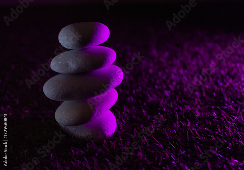 Canvas Print Mountain of white Zen stones on grass lit in white and purple