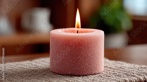 Macro Shot of a Lit Textured Pink Candle with Flickering Flame on Textured Beige Towel With a Wooden Background and Soft Lighting