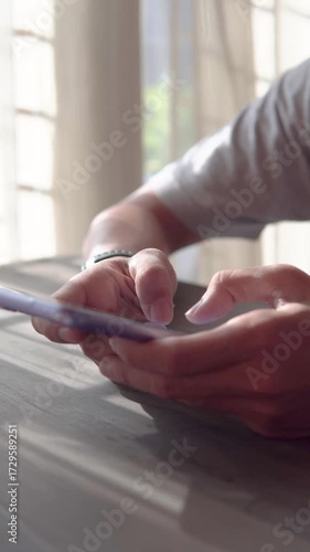 Man holding smartphone beside window while playing social media.