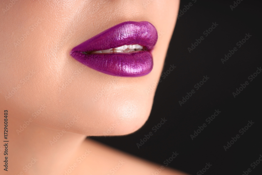 Fototapeta premium Woman with beautiful purple lipstick on her lips against black background, macro view