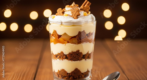 Delicious trifle dessert with layers of cake, custard, fruit, and whipped cream, garnished with cinnamon sticks on a wooden table