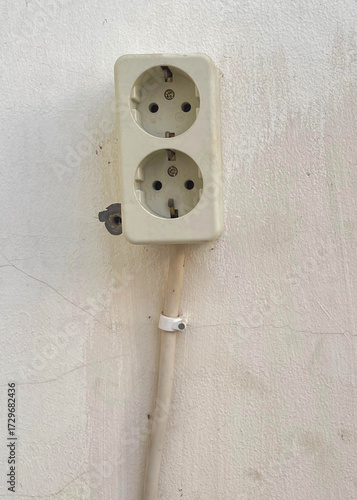 Old double electrical wall socket with power cable on white wall background, vintage electricity plug installation