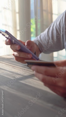 Asian man holds credit card and uses smartphone to pay for products online via the Internet.