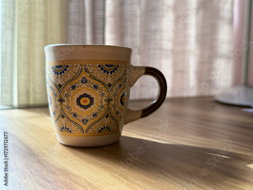 A yellow and blue cup with a floral design sits on a wooden table