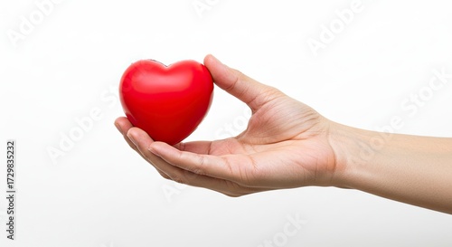 A fairskinned hand gently holds a smooth red heart against a white background