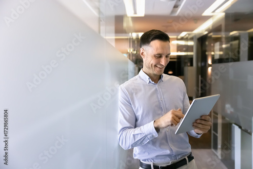 Behang Businessman standing in modern office hallway with tablet device