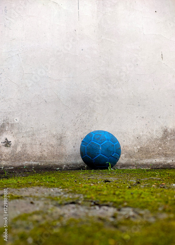 Old blue soccer ball on mossy concrete floor against vintage cracked wall grunge urban sport background texture