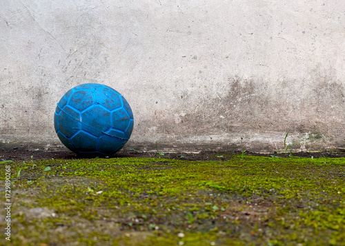 Old blue soccer ball on mossy concrete floor against vintage cracked wall grunge urban sport background texture