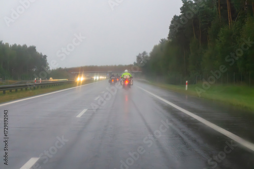 Motorcyclists riding on a highway in rain, wet road surface and limited visibility in challenging weather conditions.