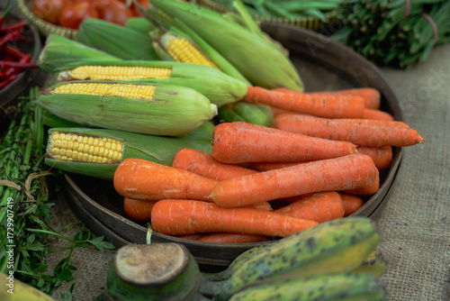 A vibrant and colorful assortment of fresh vegetables such as carrots and corn displayed beautifully in a wooden tray